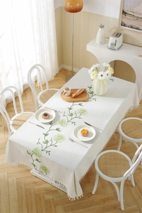 Close-up of white cotton linen tablecloth with green floral embroidery and tassels