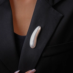 Close-up of minimalist matte silver curved brooch pinned on a black suit lapel