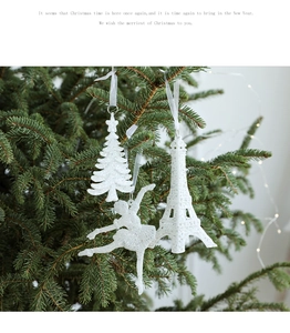 White glittery Christmas tree, ballerina, and Eiffel Tower ornaments on a pine branch