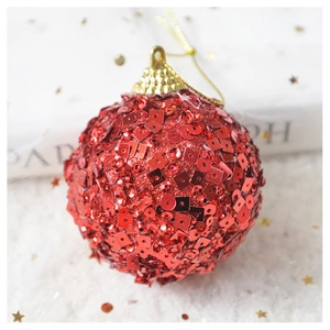 Close-up of a festive red sequined Christmas ball with gold cap on a white plush surface