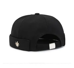 Detail view of black docker hat featuring golden leaf ornament and adjustable back strap