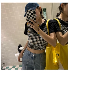 Detail view of a yellow canvas bag hanging next to a model wearing a houndstooth crop top