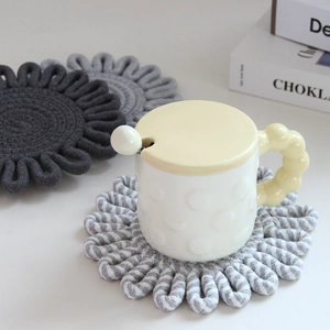 Close-up of three hand-woven cotton coasters in grey and striped flower shapes on a white table