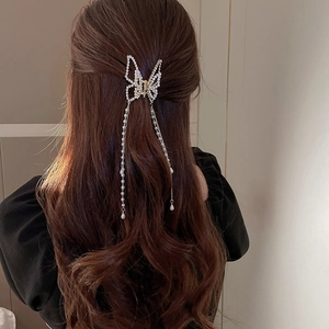 Detail of elegant gold butterfly hair claw clip with pearl tassels on dark wavy hair