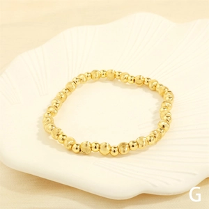 Macro view of textured and polished gold beaded stretch bracelet on white shell dish