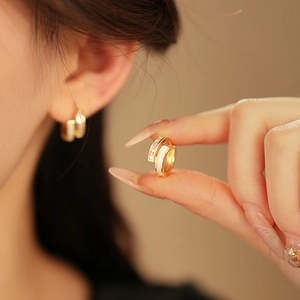 Vue rapprochée de boucles d'oreilles géométriques dorées avec émail blanc et oxydes de zirconium