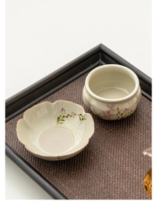Macro detail of hand-painted ceramic daisy tea strainer on a woven bamboo tray