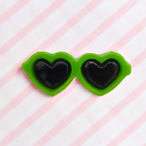 Detail of bright green heart-shaped pet glasses accessory on a striped background