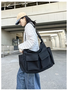 Detail of a black canvas crossbody bag featuring large front flap pockets and wide strap