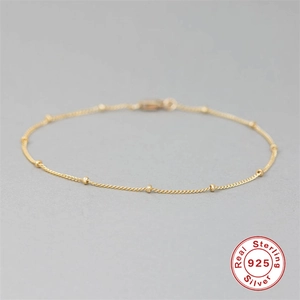 Macro detail of gold plated S925 sterling silver bead chain bracelet on grey background