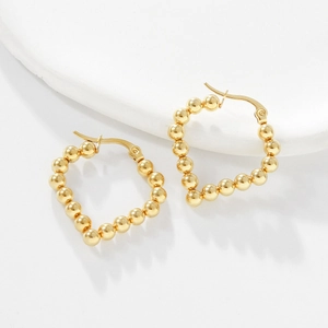 Close-up of golden beaded heart-shaped stainless steel earrings on stone stand