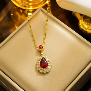 Elegant gold necklace with pear-shaped red gemstone pendant in a beige jewelry box