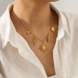 Gold stainless steel necklace with sun, Ankh cross, and shell charms worn on a person