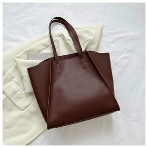 Flat lay of a large dark brown leather tote bag placed on an off-white blazer jacket