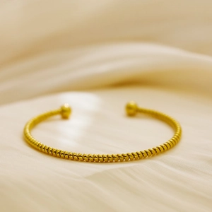 Minimalist 18k gold plated twisted rope bangle with ball ends on beige silk background