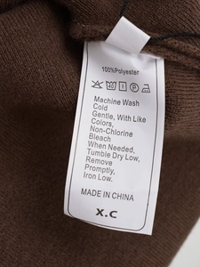 Detail of care label with 100% polyester fabric and washing symbols on a brown knit poncho