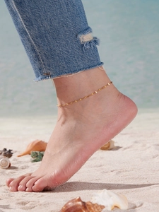 Nahaufnahme eines goldenen Schmetterling-Fußkettchens auf dem Knöchel vor Strandkulisse