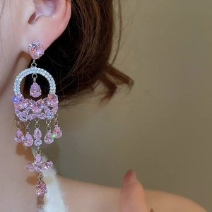 Close-up of dangling tassel earrings featuring pink heart and teardrop zircons on a model
