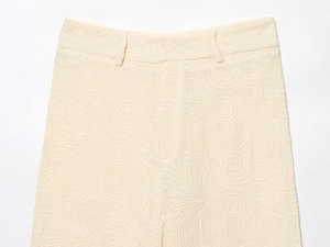 Gros plan sur la texture brodée crème et les passants de ceinture du pantalon