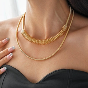 Détail d'un collier doré à deux rangs avec un design en spirale porté par un modèle