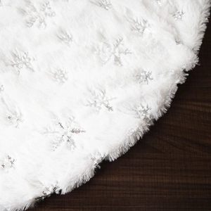 Detailed close-up of white plush Christmas tree skirt with silver sequin snowflakes