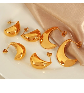 Macro view of gold teardrop earrings in three sizes on white ceramic and satin