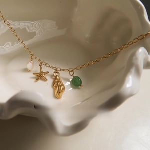 Close-up of ocean-themed charms with starfish, shell, pearl and green stone on gold chain