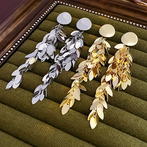 Detailed view of silver and gold leaf tassel earrings on a green velvet tray