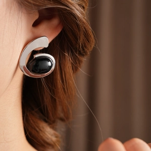 Close-up of silver S-shaped geometric earring featuring a centered black round gemstone