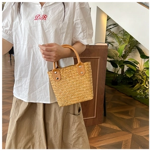 Chic brown woven straw handbag with premium leather handles and rivet details shown by model