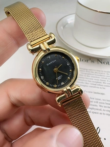 Close-up of golden vintage quartz watch with black dial and woven metal strap