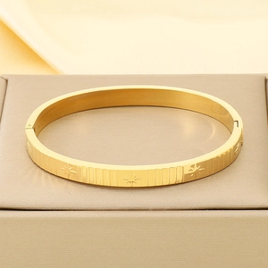 Detail view of gold bangle with star carvings and vertical stripe texture on jewelry box