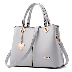 Light gray women's tote bag with golden hardware and heart charm on white background