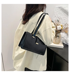 Detail view of a black glossy minimalist underarm bag on a model wearing a beige coat