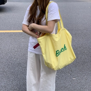 Close-up of yellow canvas tote bag with green Beach print carried by model