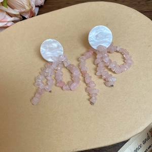 Close-up of pink natural stone tassel earrings with white shell accents on beige background