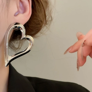 Close-up of a large polished silver heart-shaped earring worn on a model's ear