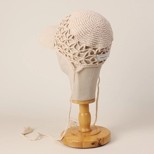 Detailed close-up of handmade hollow crochet baseball cap with tassels on wooden mannequin