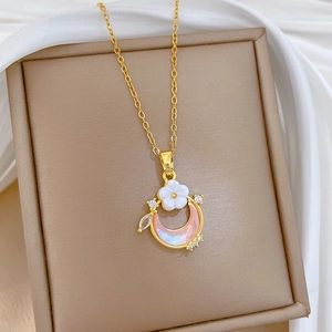 Close-up of gold moon and flower necklace with pink moon and crystals on beige jewelry box