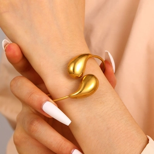 Detail of a gold teardrop open cuff bracelet with a polished mirror finish on a model