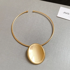 Detailed view of minimalist gold oval pendant necklace on a textured display board