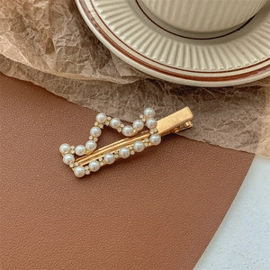 Close-up of wavy gold hair clip with white pearls and small rhinestones detail