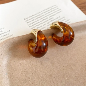 Detail of C-shaped amber resin earrings with gold metallic hardware in a vintage style