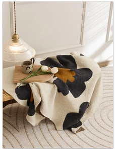 Cozy knit throw blanket with large floral patterns draped over a stylish rattan stool