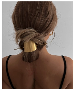 Detail view of a gold hair pin with irregular metal plate and pearl in an elegant updo