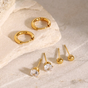 Detailed set of golden hoop earrings and cubic zirconia studs on a stone background