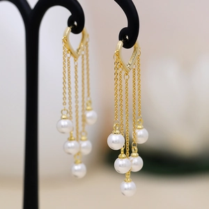 Detail of long tassel pearl earrings featuring golden heart hooks and layered chains