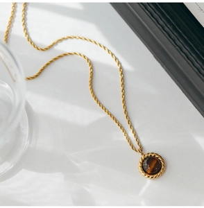 Macro detail of golden twist chain necklace with round tiger eye stone pendant