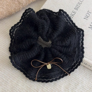 Close-up of black knitted hair scrunchie with a brown bow and metallic charm