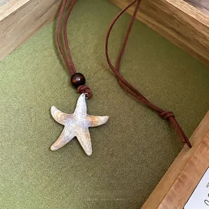 Starfish pendant necklace with brown leather cord and wood bead on a wooden tray